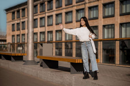 Girl standing near bench with raised hand in greetingの写真素材