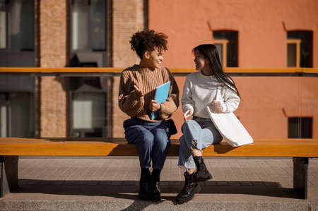 Two girls talking sitting on city benchの写真素材