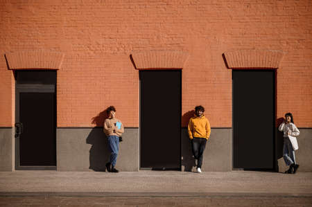 Guy and two girls standing near building waitingの写真素材