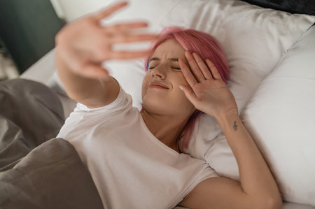 Pink-haired young girl lying in bed and looking sleepyの写真素材