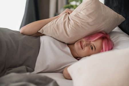Pink-haired young girl lying in bed and looking sleepyの写真素材