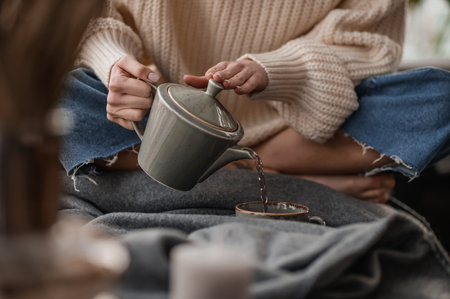 A girl in a white sweater pouring morning tea to the cupの写真素材