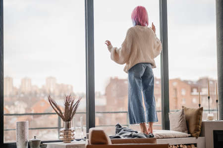 A girl with pink hair standing near the windowの写真素材