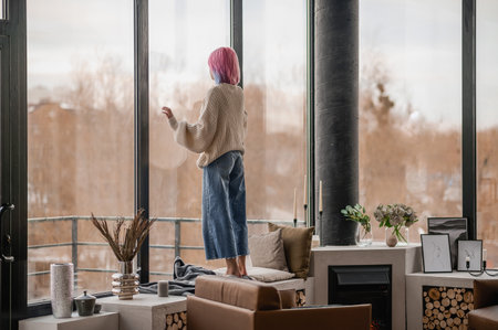A girl with pink hair standing near the windowの写真素材