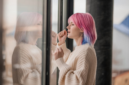 A girl with pink hair standing near the windowの写真素材