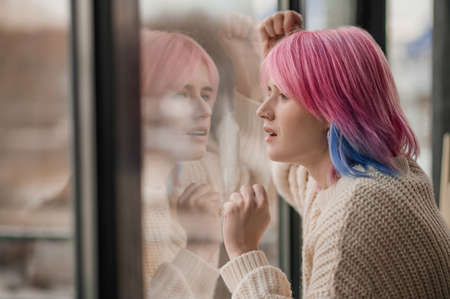 A girl with pink hair standing near the windowの写真素材