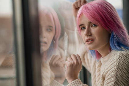 Close up of a girl with pink hair near the windowの写真素材