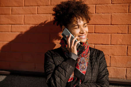 Dark-haired young girl with a phone on a brick wall backgroundの写真素材