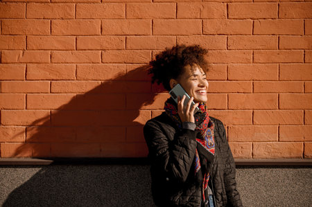 Dark-haired young girl with a phone on a brick wall backgroundの写真素材