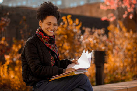 Dark-skinned girl sitting on the bench with books in handsの写真素材