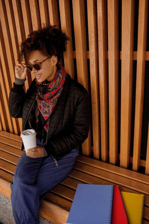 A dark-skinned girl in sunglasses with a no-spill cup in handsの写真素材