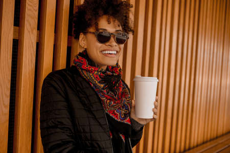 A dark-skinned girl in sunglasses with a no-spill cup in handsの写真素材
