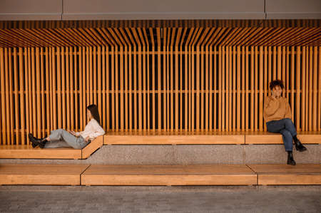 Two girls sitting in a wooden pavillion and looking busyの写真素材