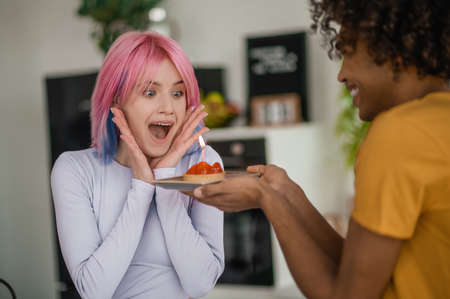 Young man holding a straberry cake with a candle, his girlgriend happyの写真素材