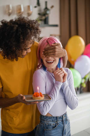 A young man closing his girlfriends eyes and holding cake in his handの写真素材