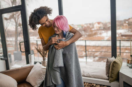 Tall young man hugging his girlfriend and covering her with a plaidの写真素材