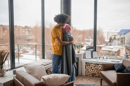 Tall young man hugging his girlfriend and covering her with a plaidの写真素材