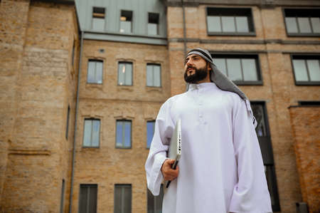 An arabian man in traditional clothing with a laptop in the streetの写真素材