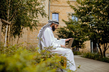An arabian man in traditional clothing with a laptop in the streetの写真素材