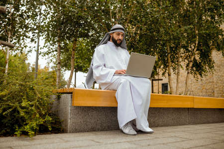 An arabian man in traditional clothing working on a laptop outsideの写真素材