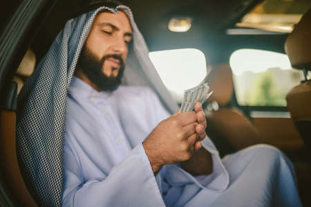 An arabian man in a traditional clothing in a car holding moneyの写真素材