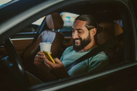 Young handsome dark-haired man holding a phone and driving a carの写真素材