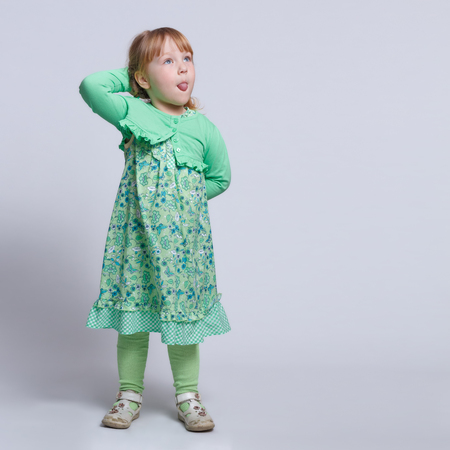 A little girl standing with hands behind her back and sticking out her tongueの写真素材