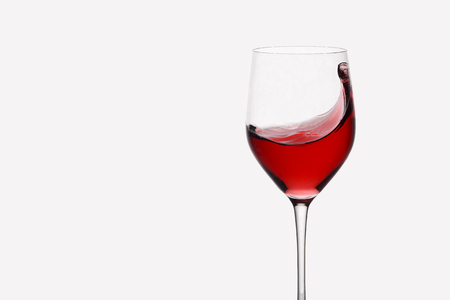red wine swirling in a wine glass standing against light backgroundの写真素材
