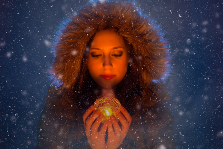 Young woman with magic light in hands at night during a snowstormの写真素材
