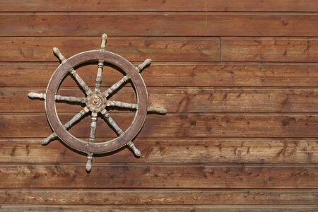Old ship steering wheel hangs on the wooden wallの写真素材