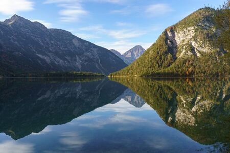 Mountains are reflected in the water of a mountain lake. The picture is taken in Alps at Plansee in Tirolの写真素材