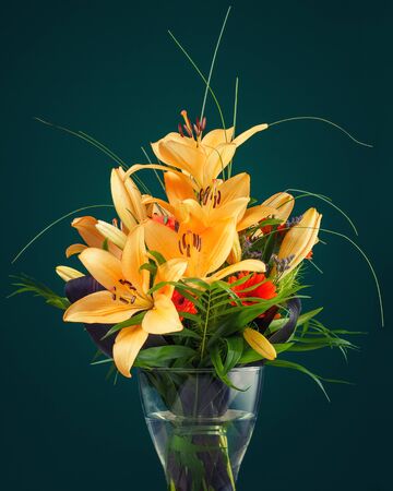 A bunch of yellow lily flowers in a vase on a table against a green wallの写真素材