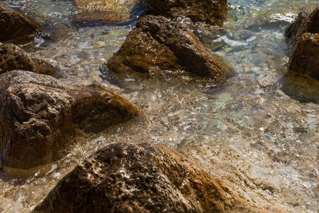 A wave rolls on large stones on the beachの写真素材