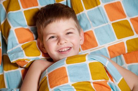 Cheerful boy in bed does not want to sleep
