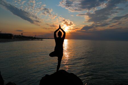 silhouette of yoga asana tree at sunrise on the seashoreの写真素材