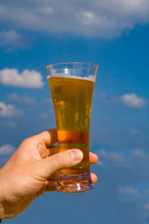 Hand with a glass of beer on the background of the blue summer sky.