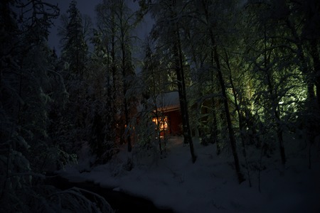 House with light in window among night, snowy winter forest, Finlandの写真素材