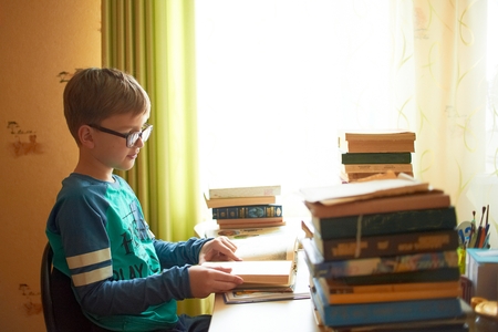 education, childhood, people, homework and school concept - bored student boy reading book or textbook at homeの写真素材