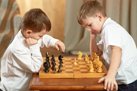 two boys dressed in white are playing chess on the tableの写真素材