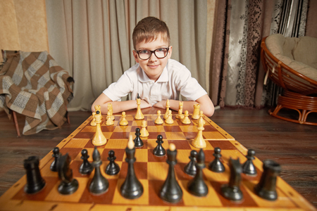 boy with glasses in a white shirt playing chess making a move holding the figure smilesの写真素材