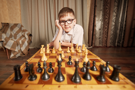 boy with glasses in a white shirt playing chess making a move holding the figure smilesの写真素材