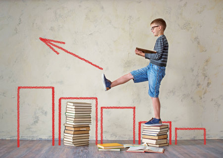 The boy student in sneakers shorts and a sweater sitting on a stack of books and reading. On a yellow colored background. Educational conceptの写真素材