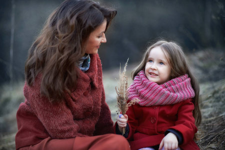 girl the daughter and mother in a red coat skirt the field on the grass in the forest at sunset