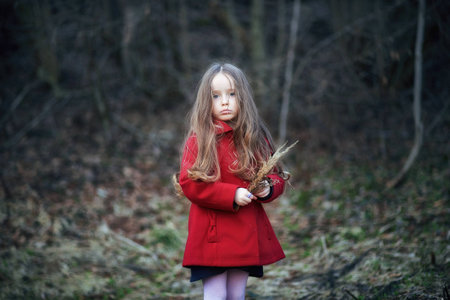 little girl in red coat, cute, beautiful, pretty, boots with the flower stands in a field at sunsetの写真素材