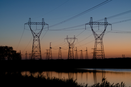 Many pillars of a high-voltage power line with wires in the steppe at dawn against the background of...