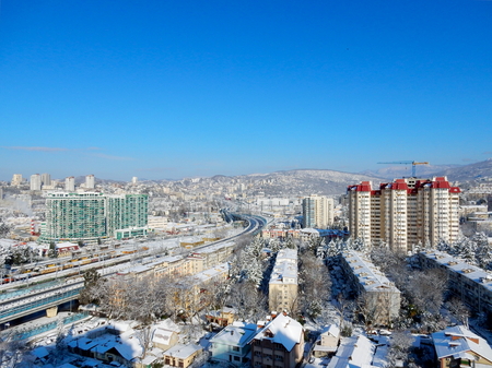 Snow-covered houses and buildings in the city, taken from the top (from a height). Blue sky over the city. Mountains in the city. Winter in the cityの写真素材