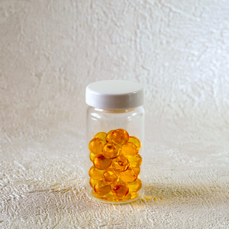 Transparent round capsules in a transparent glass jar on a light textured backgroundの写真素材