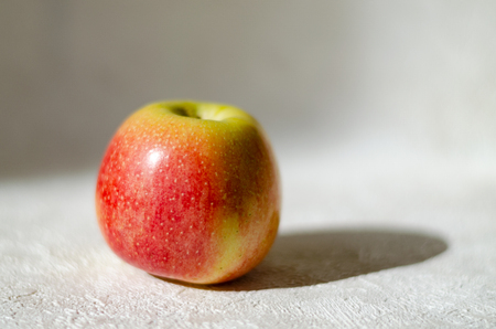 Red apple on a textured surface with lighting to the left, glare from the sun and shadow. Single itemの写真素材