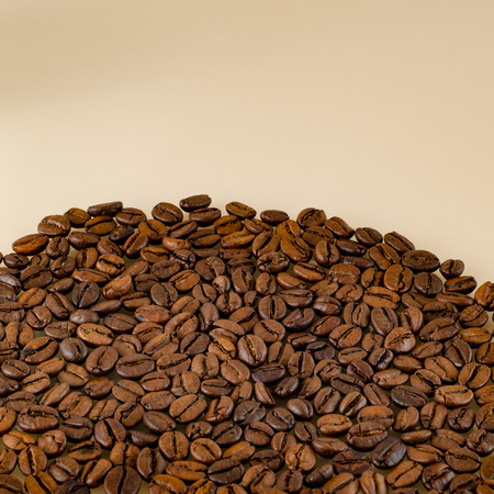 Close-up coffee beans at the bottom of the picture on a matte beige surfaceの写真素材