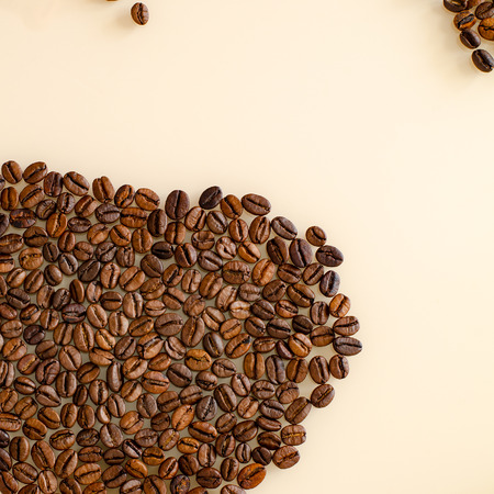 Close-up coffee beans in the lower left corner with particles on top, on a matte surface of beige colorの写真素材